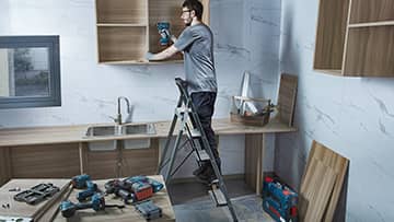 一名男子在现代厨房中使用博世工具安装架子。