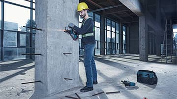 一名戴着黄色安全帽的工人在钻一个混凝土柱子。