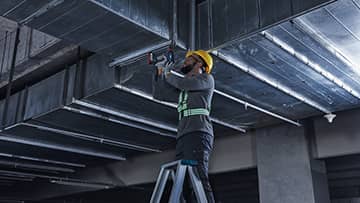 一个工人在梯子上将金属部件安装在天花板上。