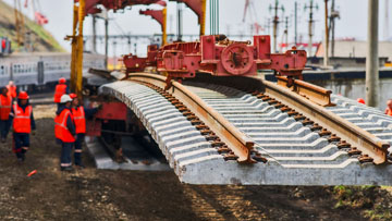 穿着橙色衣服的工人正在用起重机铺设轨道。