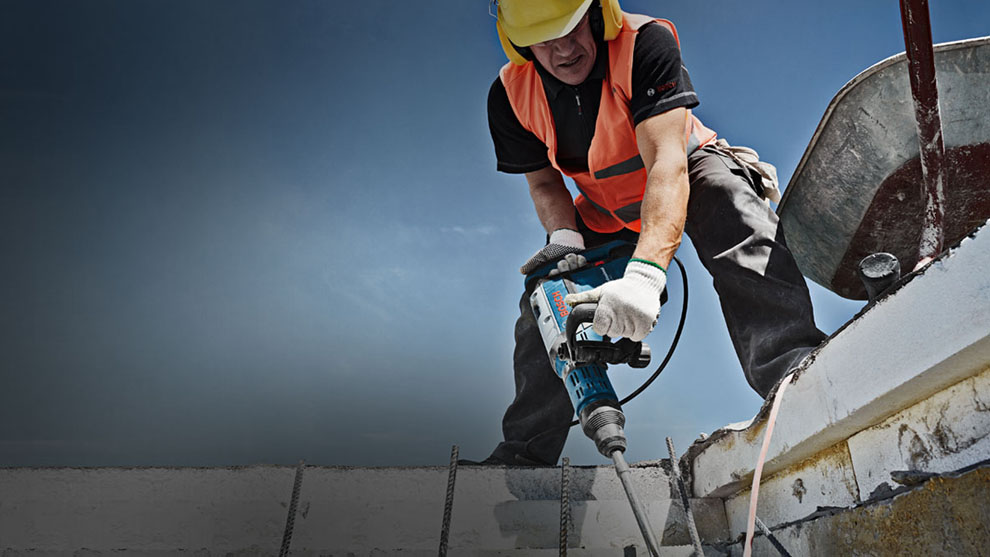 穿着警示背心的工人在建筑工地上使用博世电锤。