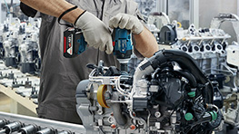 一名戴着安全帽和防护口罩的工人在脚手架上使用电钻。