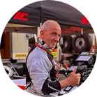 一个戴着头盔和赛车服的男人在帐篷和工具前竖起大拇指。